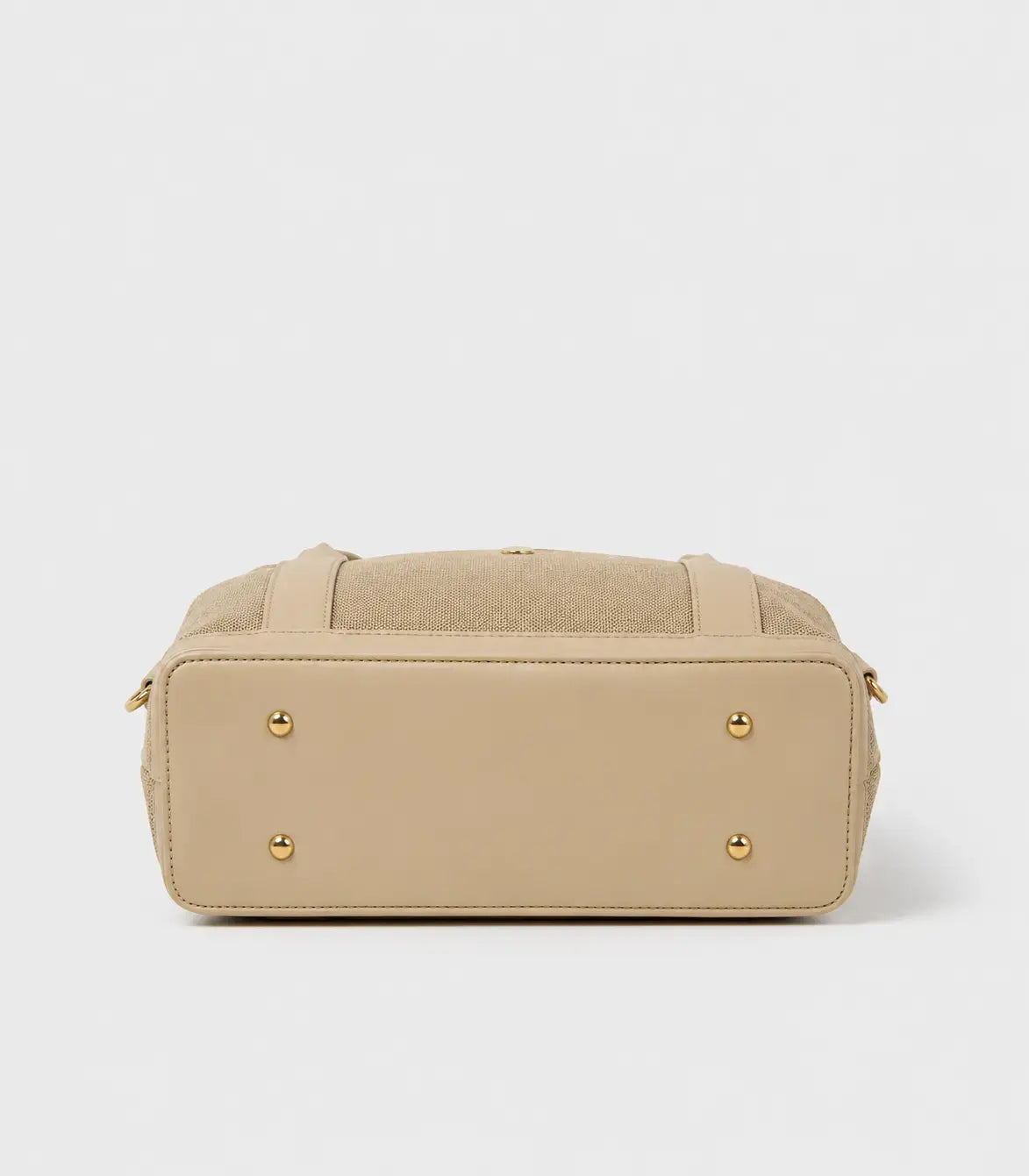 A beige handbag shown from the back, featuring a smooth leather base, a textured fabric top panel, and four gold-tone metal studs on the back corners.