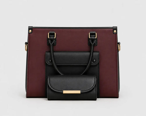 A structured handbag in burgundy and black faux leather, featuring a front flap pocket with a smaller matching black pouch attached in front, set against a plain light gray background.