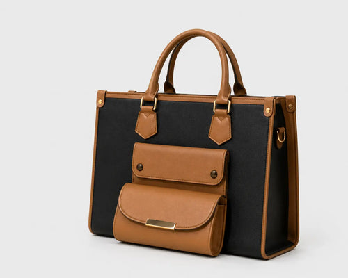 A structured tote bag with a black canvas body and tan leather trim, handles, and front pocket, shown on a light gray background.