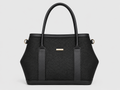 A structured black handbag with a woven texture, dual top handles, vertical leather side panels, and a small gold-tone rectangular logo plaque on the front, shown against a light gray background.