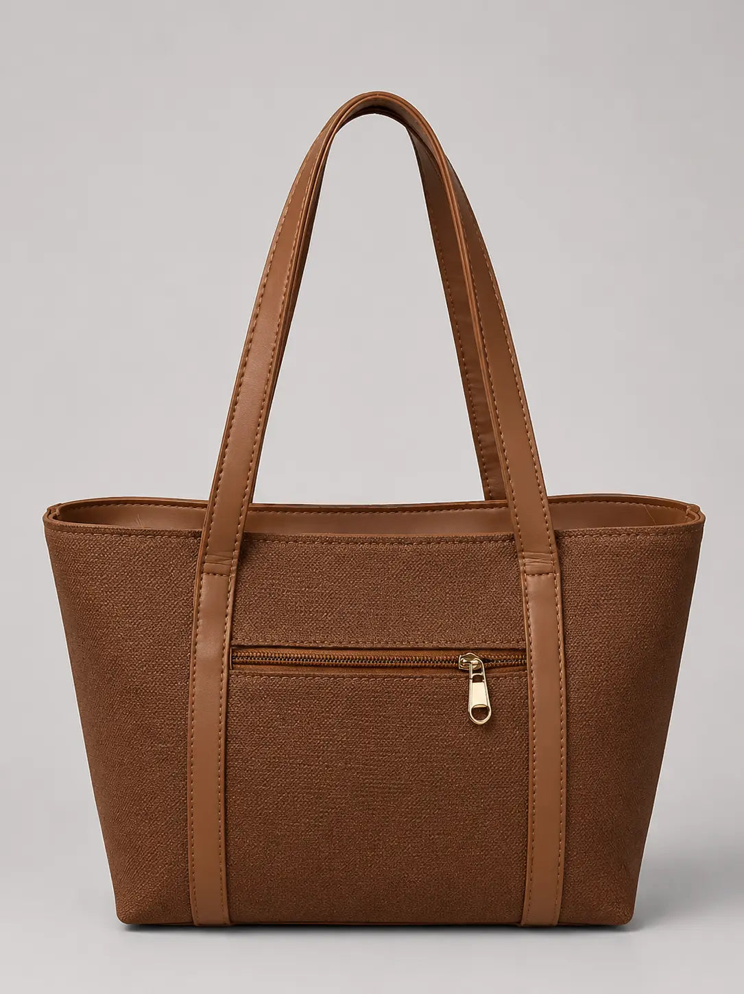 A brown faux-leather tote bag with a textured canvas-like front panel, dual top handles, and a front zippered pocket with a gold-tone zipper pull, shown against a neutral gray background.