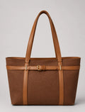 A structured brown tote bag with tan leather handles, trim, and a central buckle strap detail, photographed against a neutral light gray background.