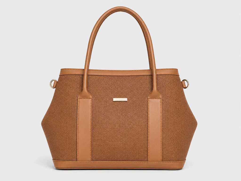 A structured tan tote bag with a woven brown body, smooth tan leather trim, dual top handles, and a small gold-tone logo plaque on the front, shown against a light gray background.