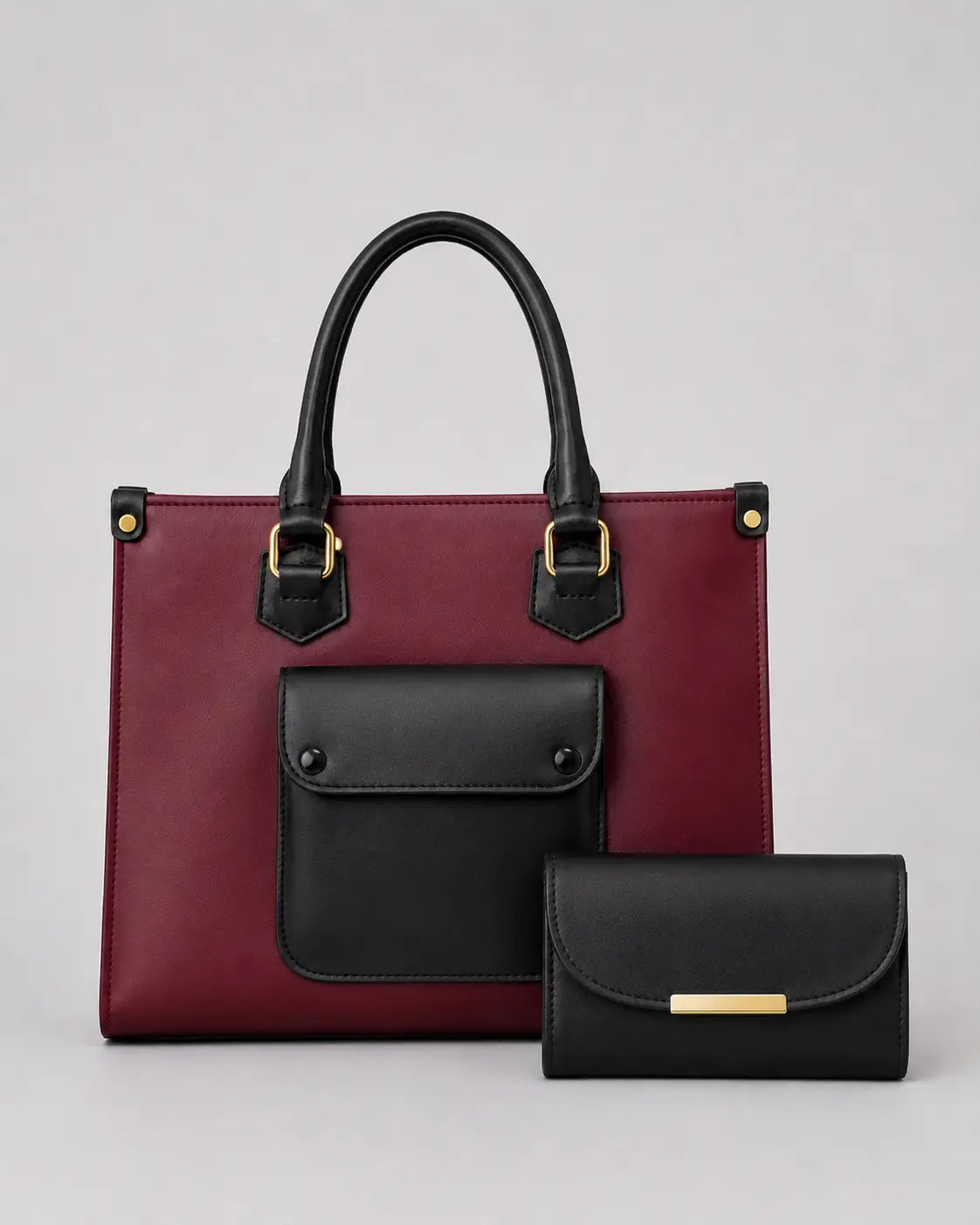 A structured tote bag in burgundy and black leather with gold-tone hardware, shown alongside a matching black wallet on a light gray studio background.