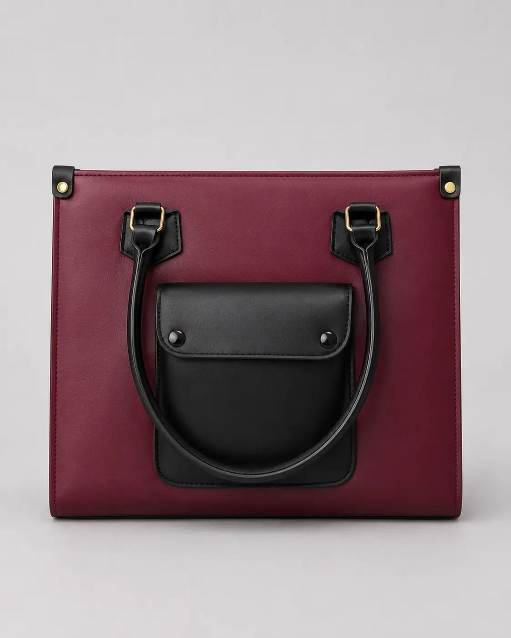 A structured tote bag in deep burgundy with a contrasting black front pocket and black leather handles, shown against a neutral light gray background.