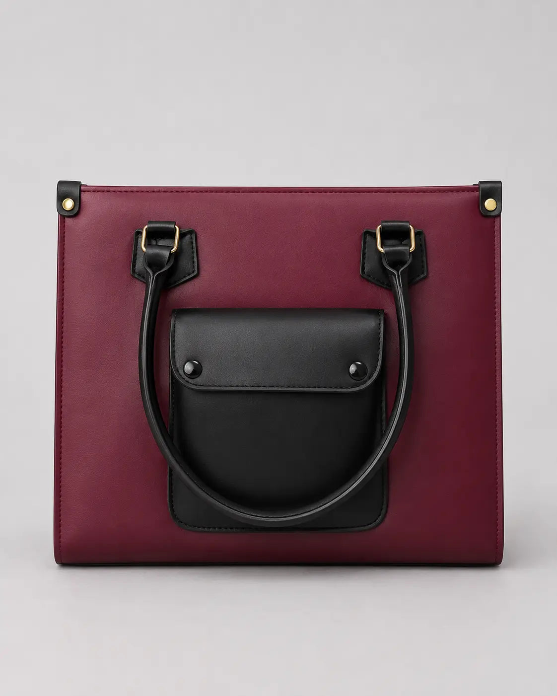A structured tote bag in deep burgundy with a contrasting black front pocket and black leather handles, shown against a neutral light gray background.