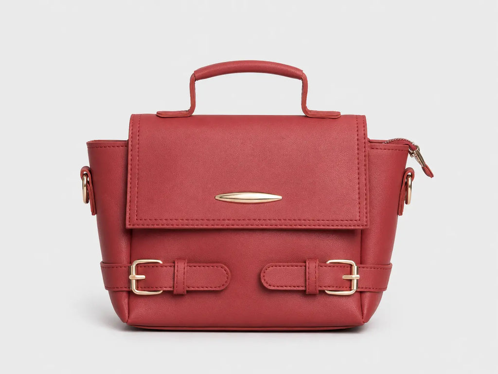 A structured red leather handbag with a top handle, gold-tone buckle straps on the front, and a zippered side pocket, shown against a light gray background.