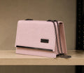 Pink handbag with a chain strap on a wooden surface against a beige background
