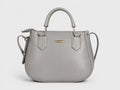 A light gray leather handbag with a top handle, shoulder strap, and gold-tone hardware, shown against a plain light gray background.