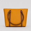 A mustard yellow tote bag with brown leather handles and trim, shown against a neutral light gray background.