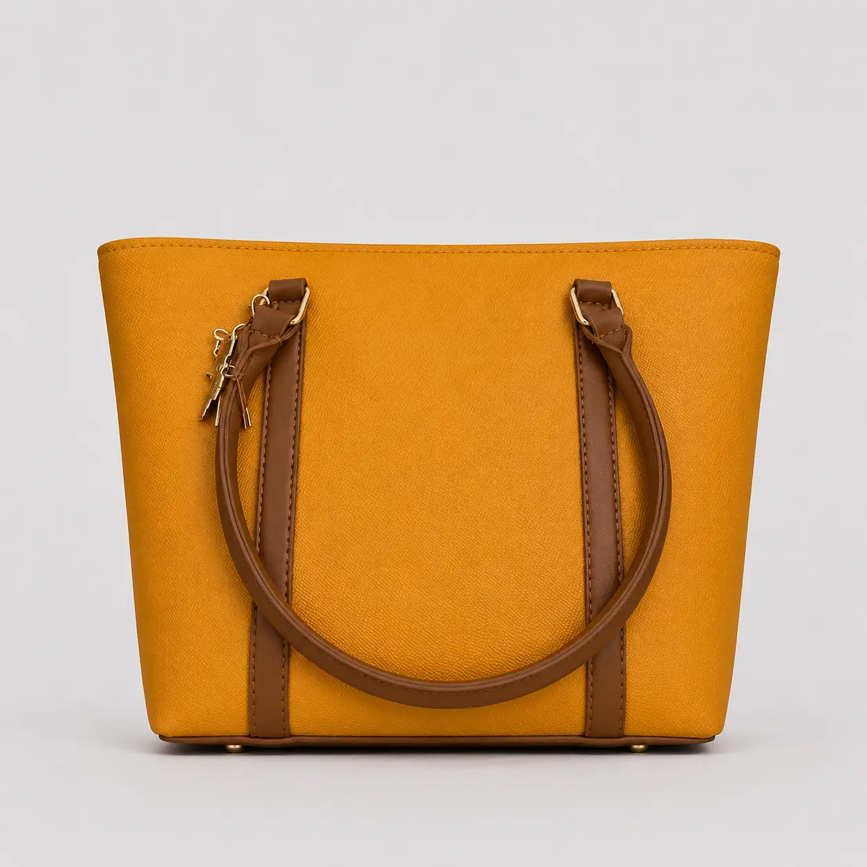 A mustard yellow tote bag with brown leather handles and trim, shown against a neutral light gray background.