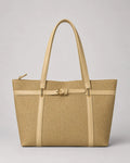 A structured tote bag in a woven beige texture with smooth beige leather trim, double shoulder straps, and a decorative buckle detail on the front, shown against a neutral light gray background.
