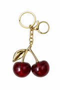 A cherry keychain featuring two glossy red glass cherries attached to gold-tone metal stems, rings, and a lobster clasp, shown on a plain white background.