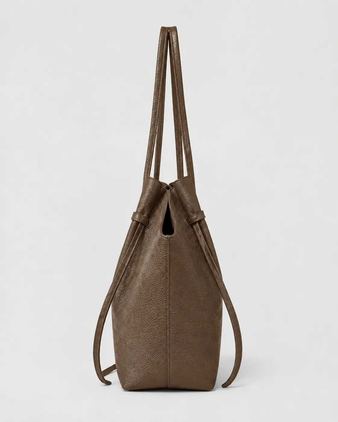 A brown textured leather bucket bag with long shoulder straps, shown from the back against a light gray background.