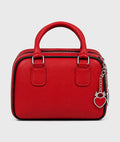 A red textured leather handbag with a top handle, silver-tone hardware, and a dangling heart-shaped padlock charm, shown against a light gray background.